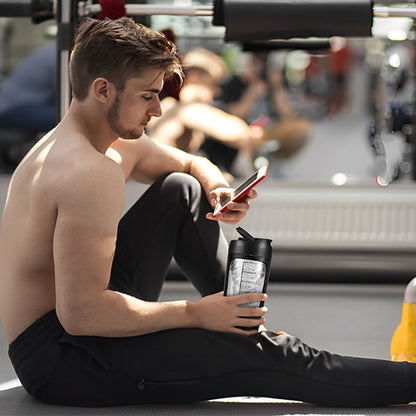 homme regarde smartphone qui tient shaker proteine